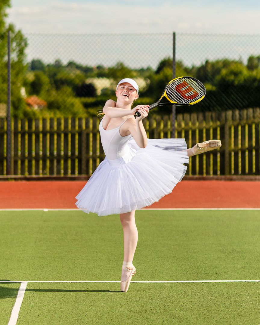 Ballet dancer in white tutu performs elegant pose with tennis racket on outdoor court.
