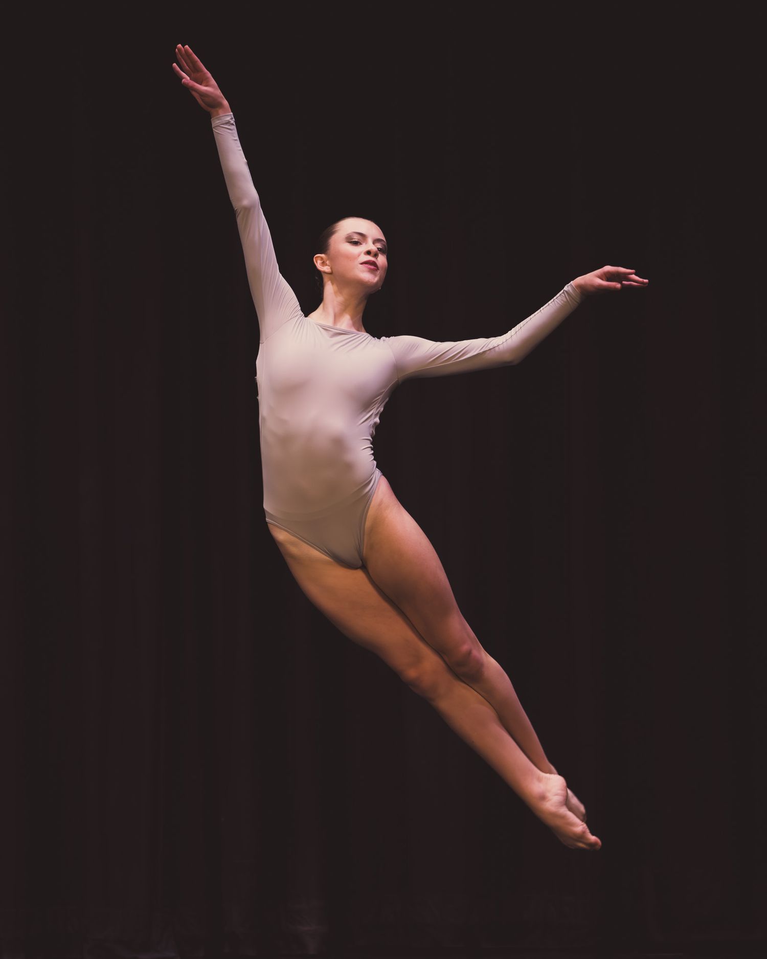 Graceful dancer leaps through air in minimalist performance on dark stage.