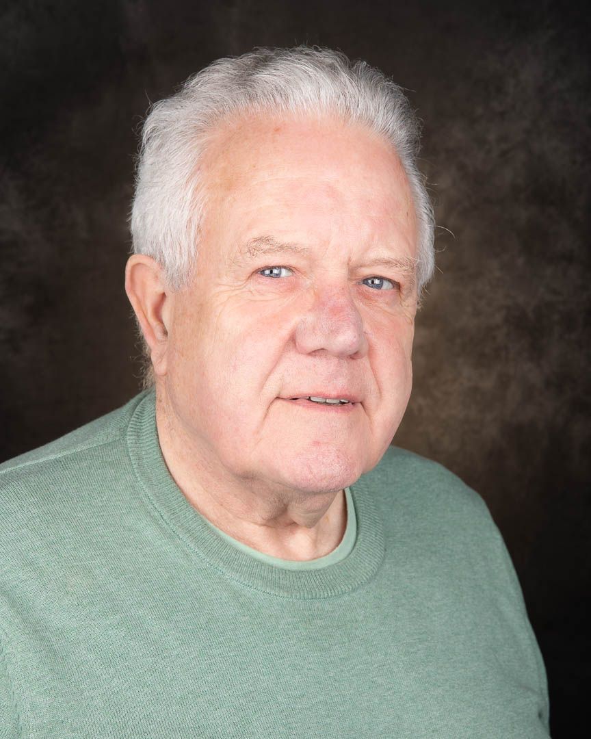 Elderly man with white hair wearing a green sweater, posing for a professional portrait photo.
