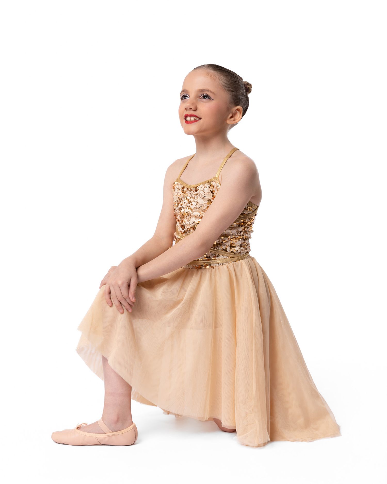 Graceful dancer in peach-colored dress poses elegantly on studio floor.