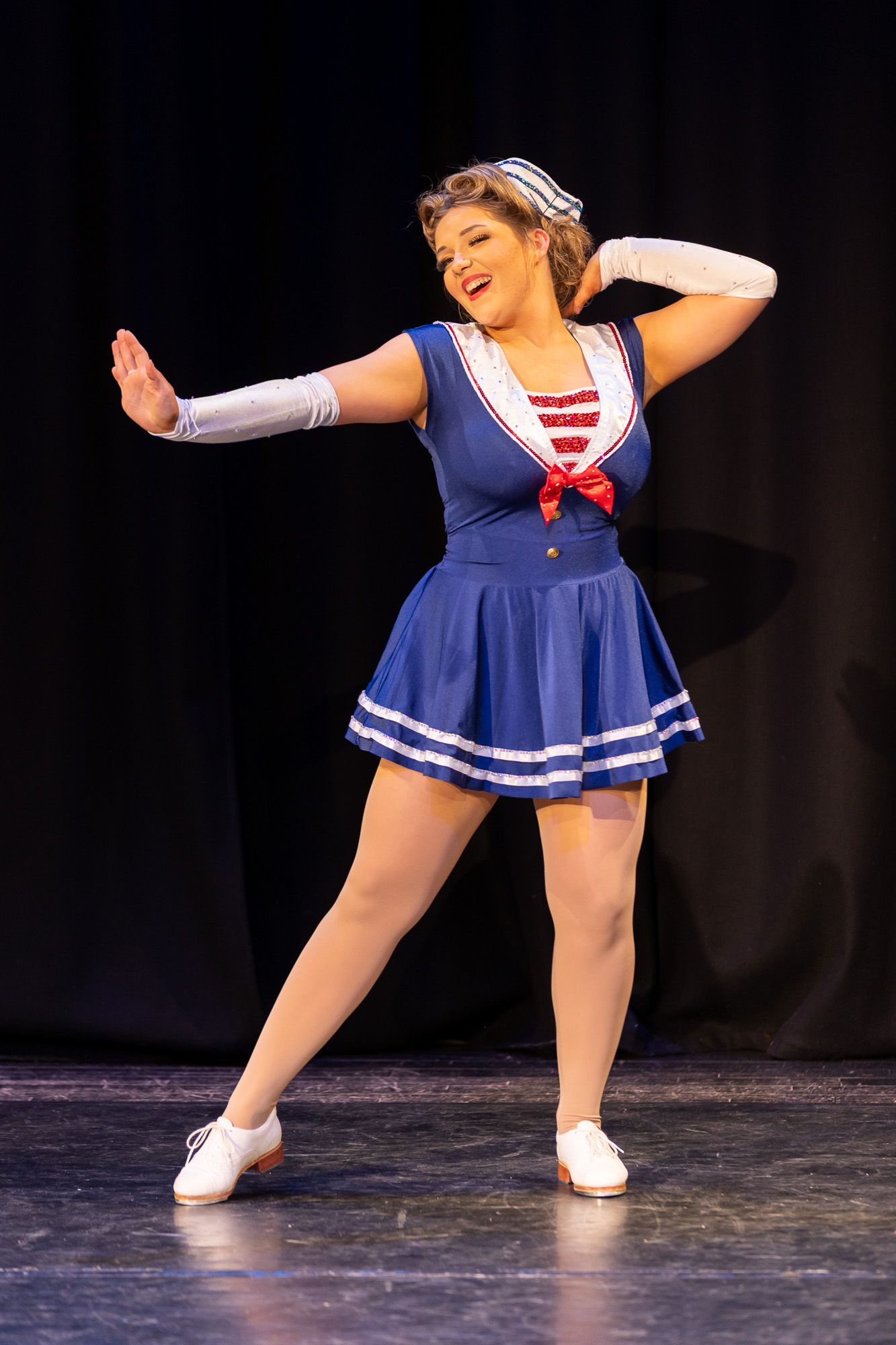 Female dancer in blue sailor costume performing on stage with white gloves and tap shoes.