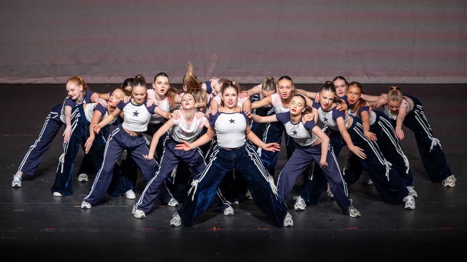A dance team in navy blue and white uniforms performs a synchronized routine on a dark stage.