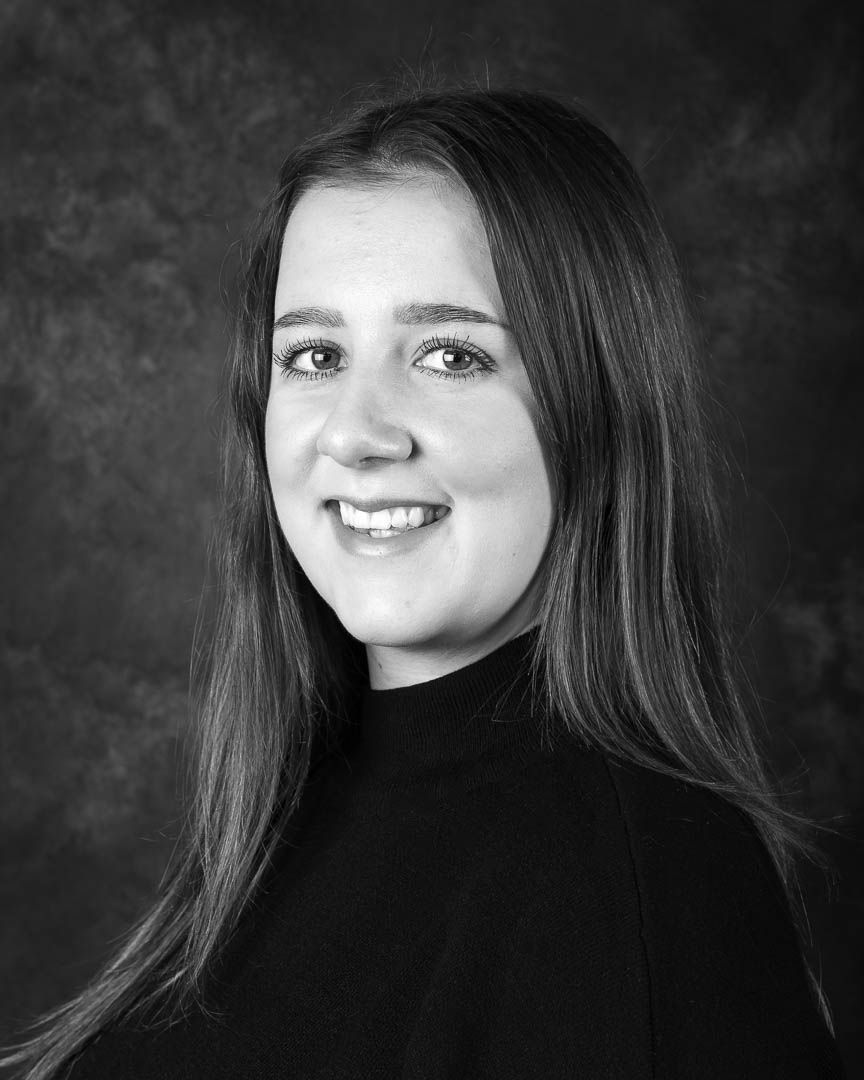Professional black and white headshot of a young woman with long hair wearing a turtleneck sweater.