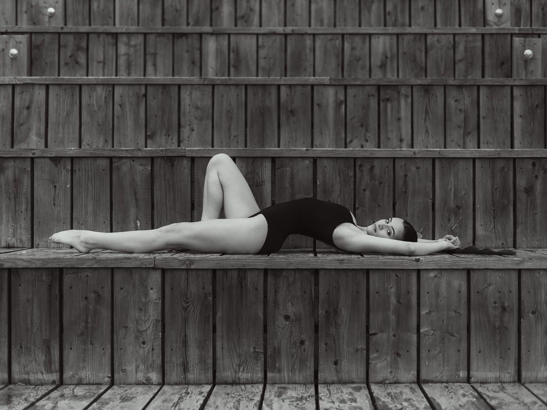 Black and white photo of a woman in a swimsuit lying gracefully on wooden bleachers.