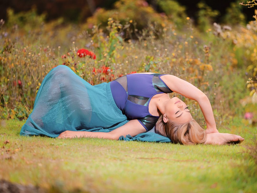 Dancer in blue outfit reclines on grass during outdoor photo session.