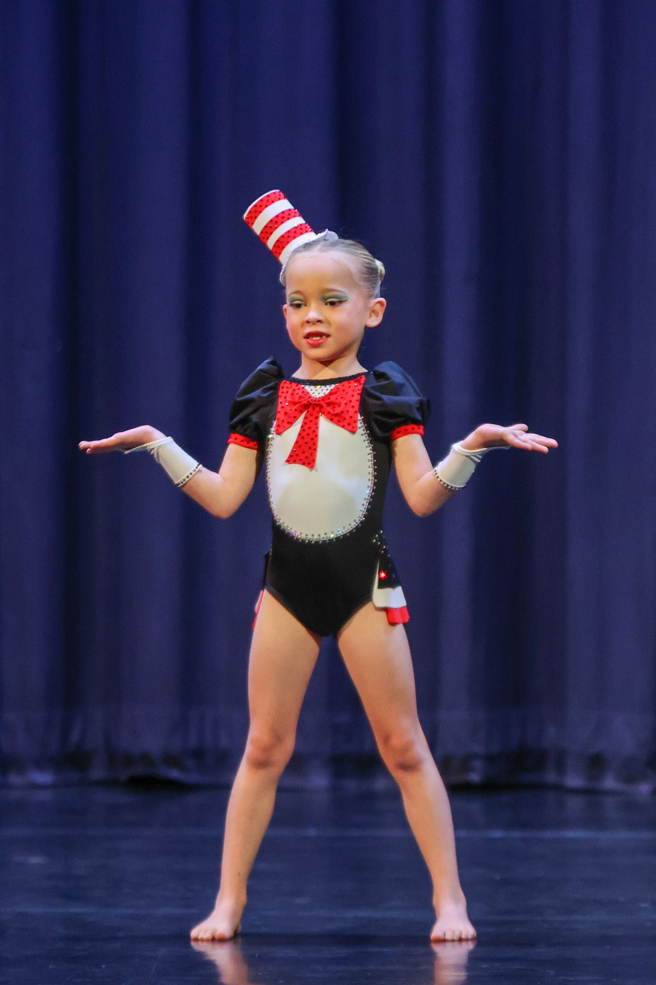Young girl performs on stage in Cat in the Hat costume with striped hat and black leotard during dance recital.