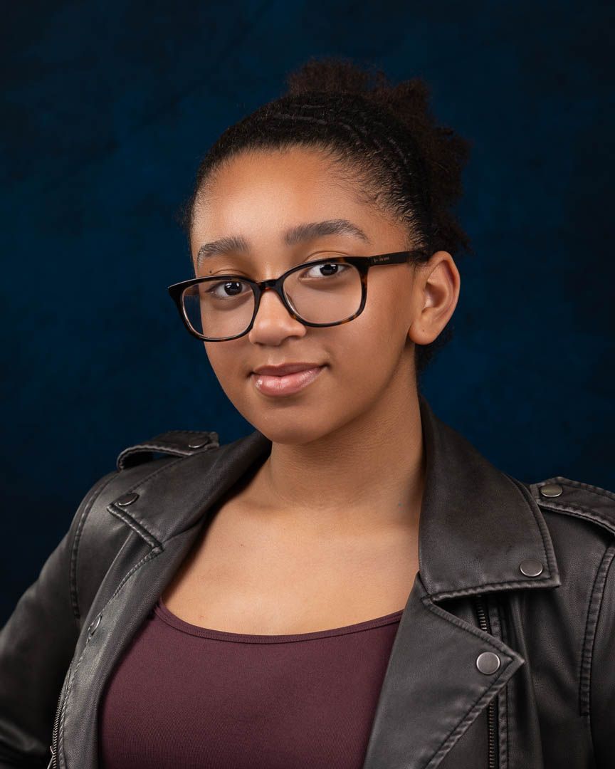 Young woman with glasses and dark hair wearing a leather jacket poses for a professional portrait photo.