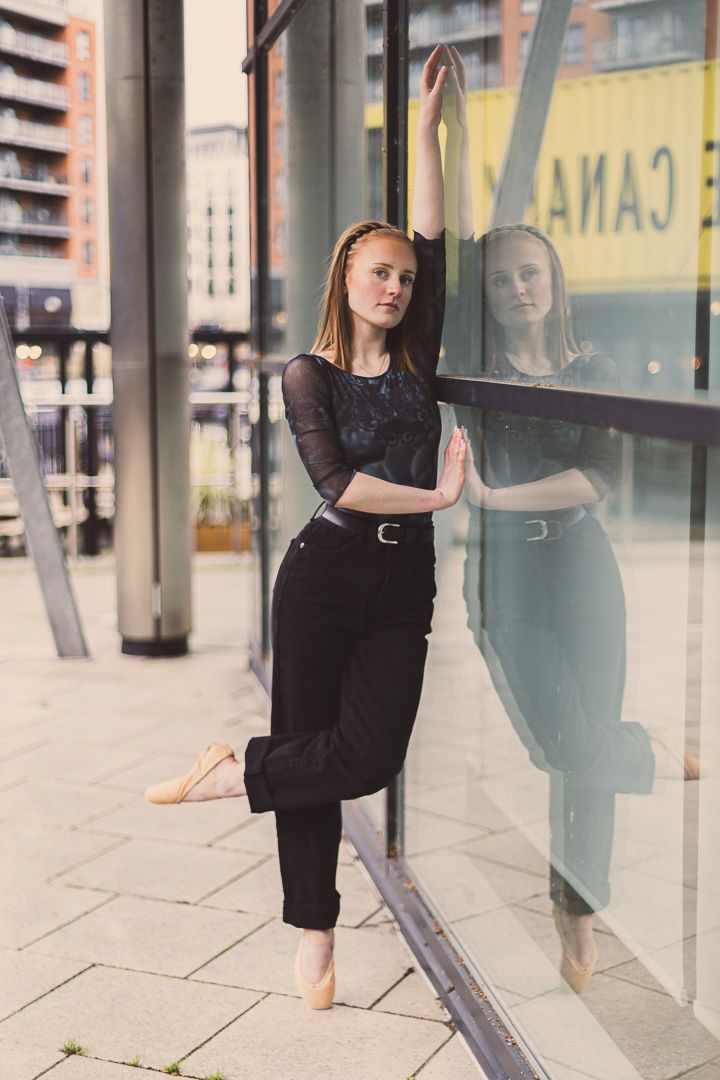 Modern dancer performs against reflective glass storefront in urban setting.