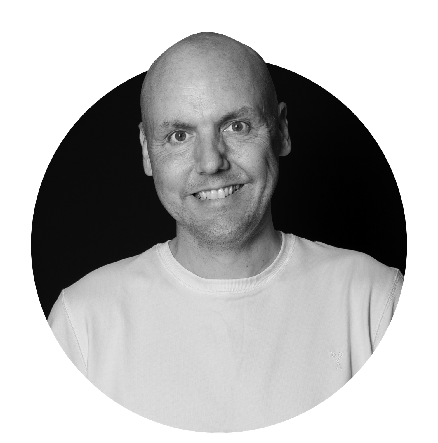 Black and white portrait of a smiling bald man wearing a white t-shirt against a dark background.