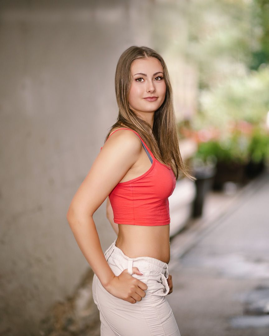 Person in coral crop top and beige high-waisted pants poses outdoors with blurred natural background.