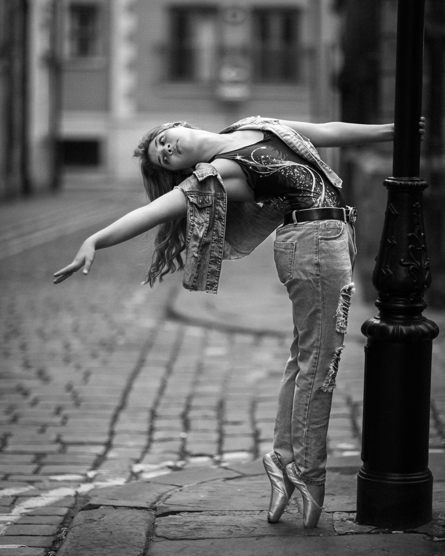 Black and white sequence showing a person in jeans bending backwards against a lamp post on a cobblestone street.