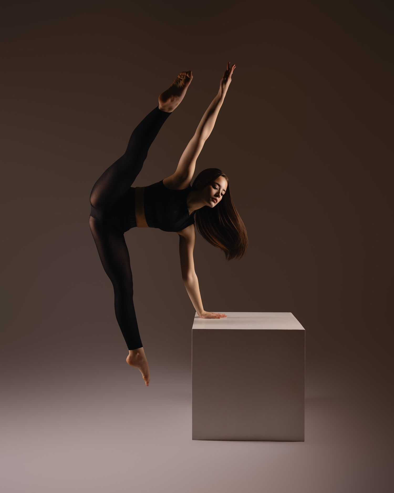 A dancer performs a graceful sequence of contemporary movements on a minimalist white platform against a dark background.