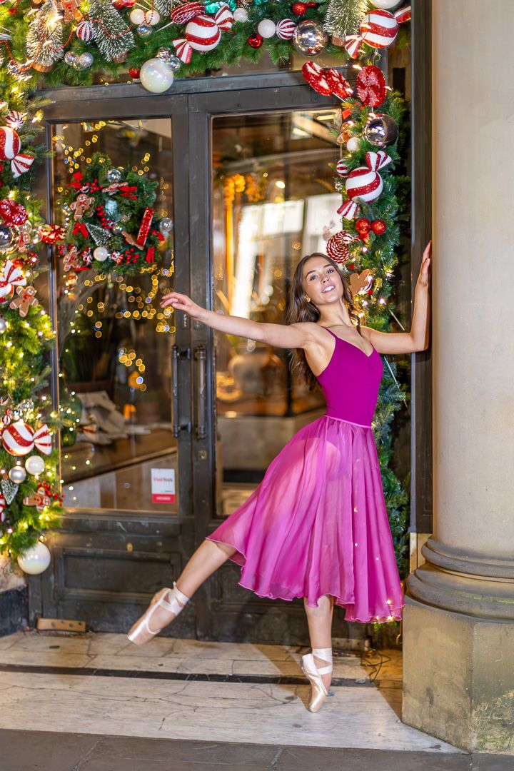 Ballerina in pink dress performs elegant poses by festive Christmas decorations.