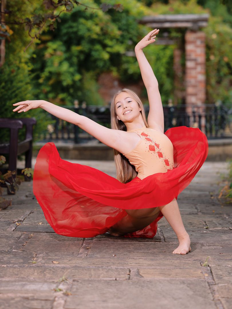Flowing red fabric creates dramatic movement in dance sequence on stone pavement.