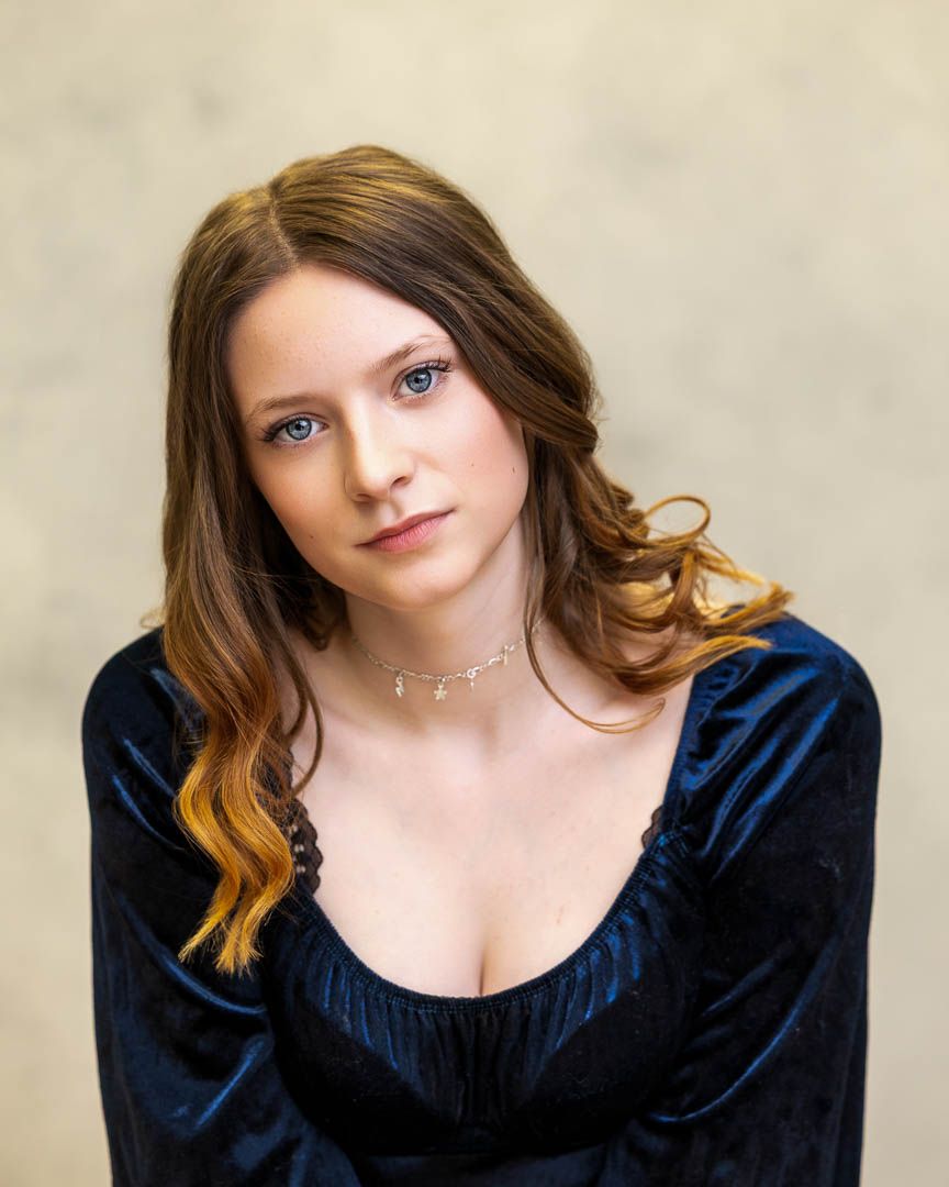Young woman with auburn hair in blue velvet dress wearing a delicate choker necklace poses for portrait photo.