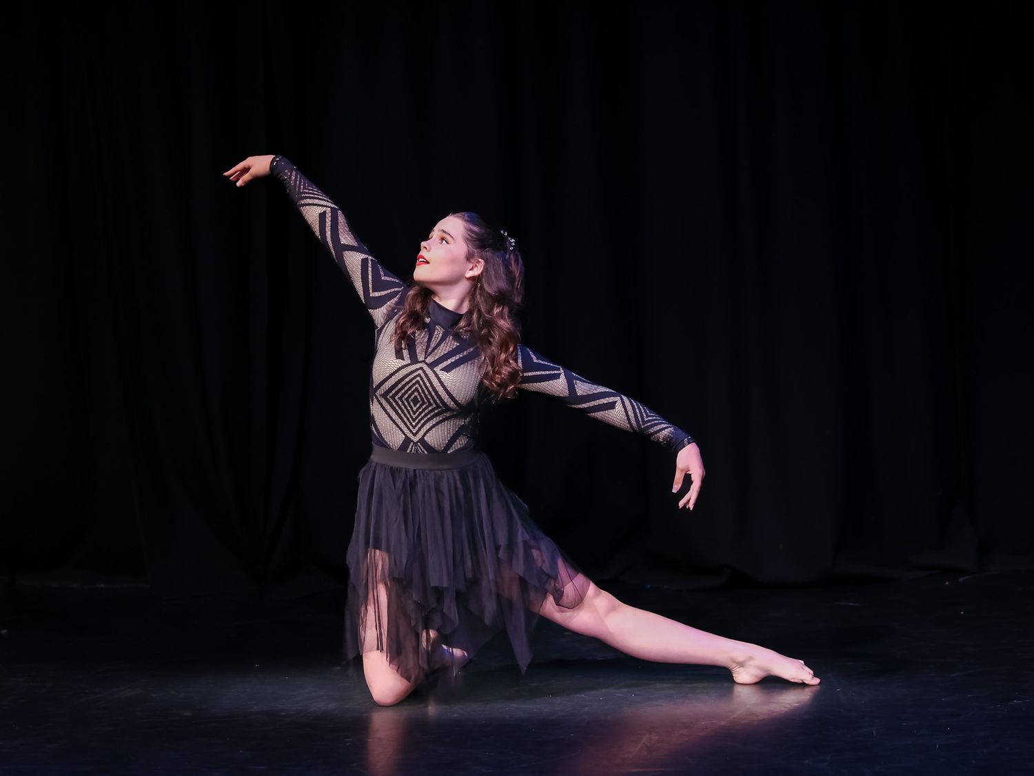 Graceful dancer performs an elegant contemporary ballet pose on stage in a black geometric costume.