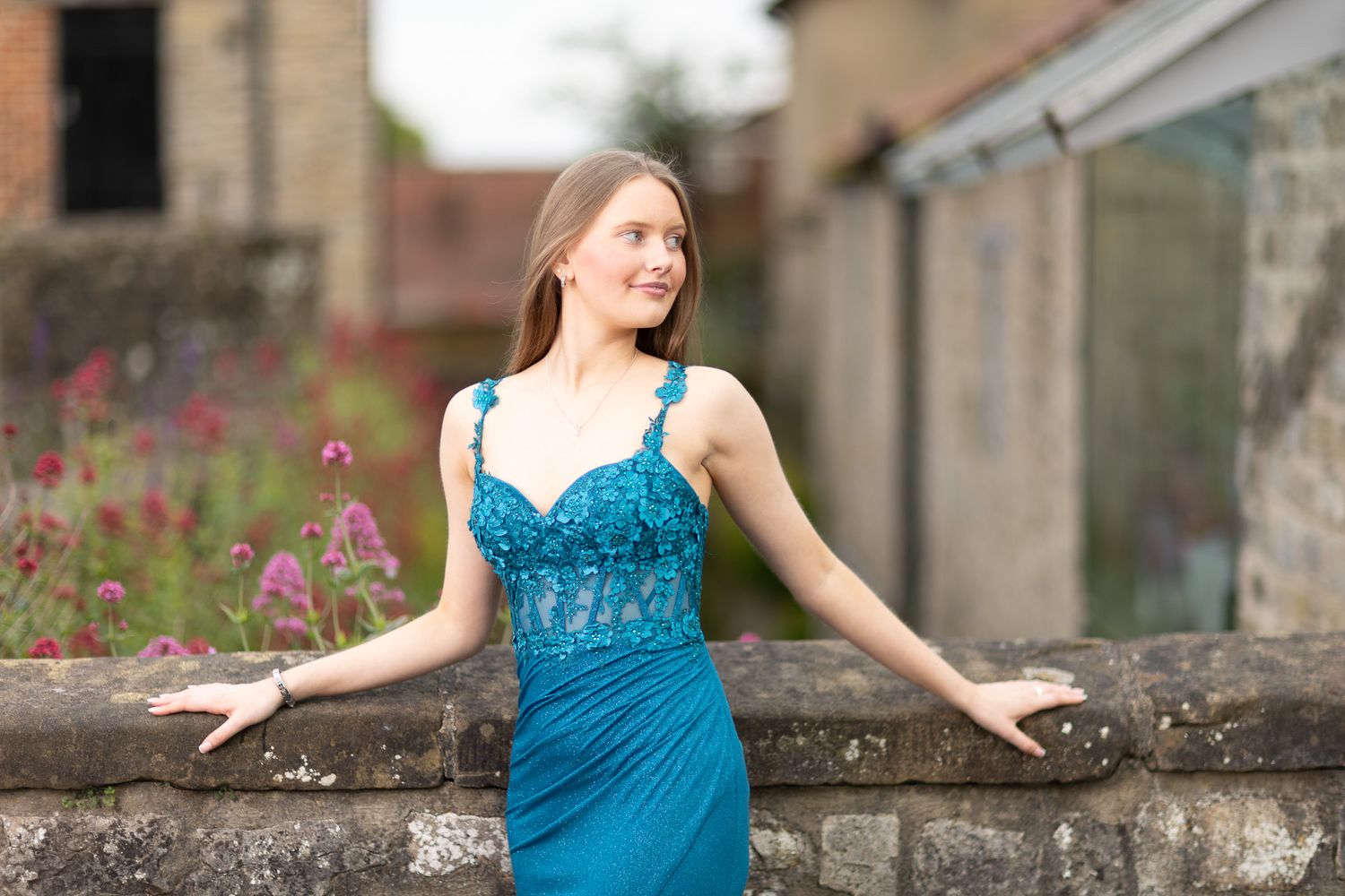 Graceful poses in a teal gown against architectural backdrop with flowers.
