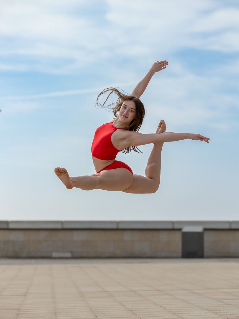 Dancer performs aerial leap against blue sky on concrete surface.