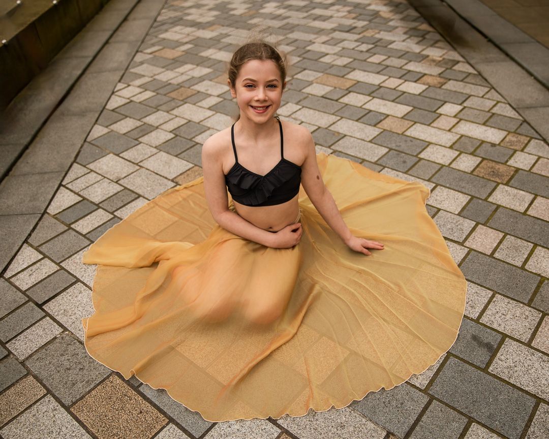 Dancer in black top with flowing gold skirt posed on patterned stone pavement.