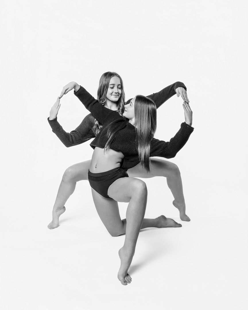 Two dancers in black outfits perform a synchronized modern dance pose in black and white photography.