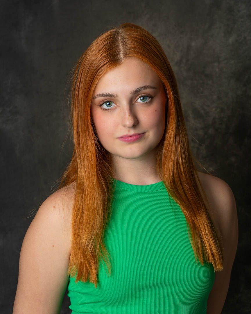 Young woman with long red hair and green eyes wearing a green sleeveless top, posing for a portrait photo.