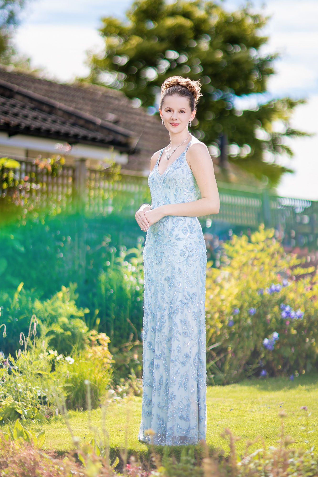 Someone wearing a light blue floral dress poses in a sunny garden with yellow wildflowers.