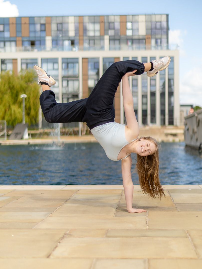 Young gymnast performing a one-handed cartwheel on a waterfront plaza with modern buildings in the background.