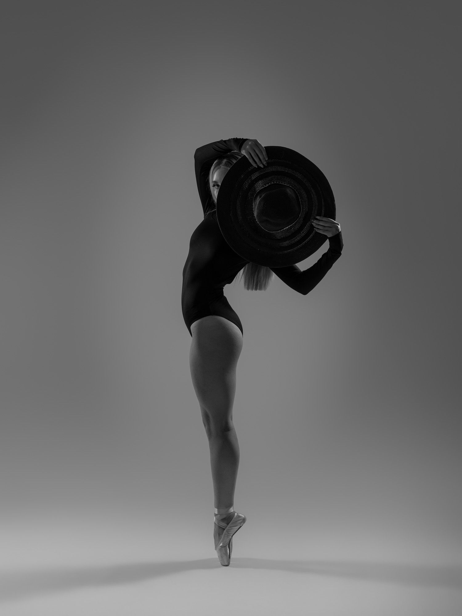 Black and white photo of a ballerina on pointe holding a large camera lens, showcasing grace and artistry.