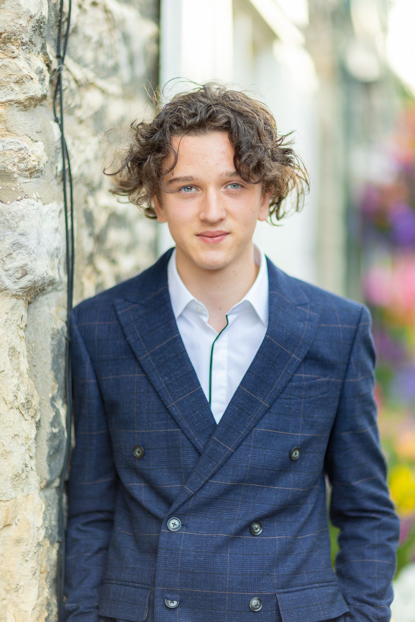 Portrait against stone wall wearing navy double-breasted suit and white shirt.