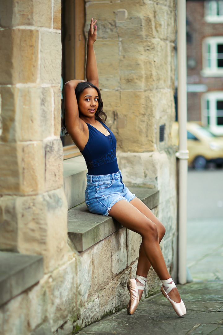 Ballet dancer performs graceful pose against stone pillars in urban setting.