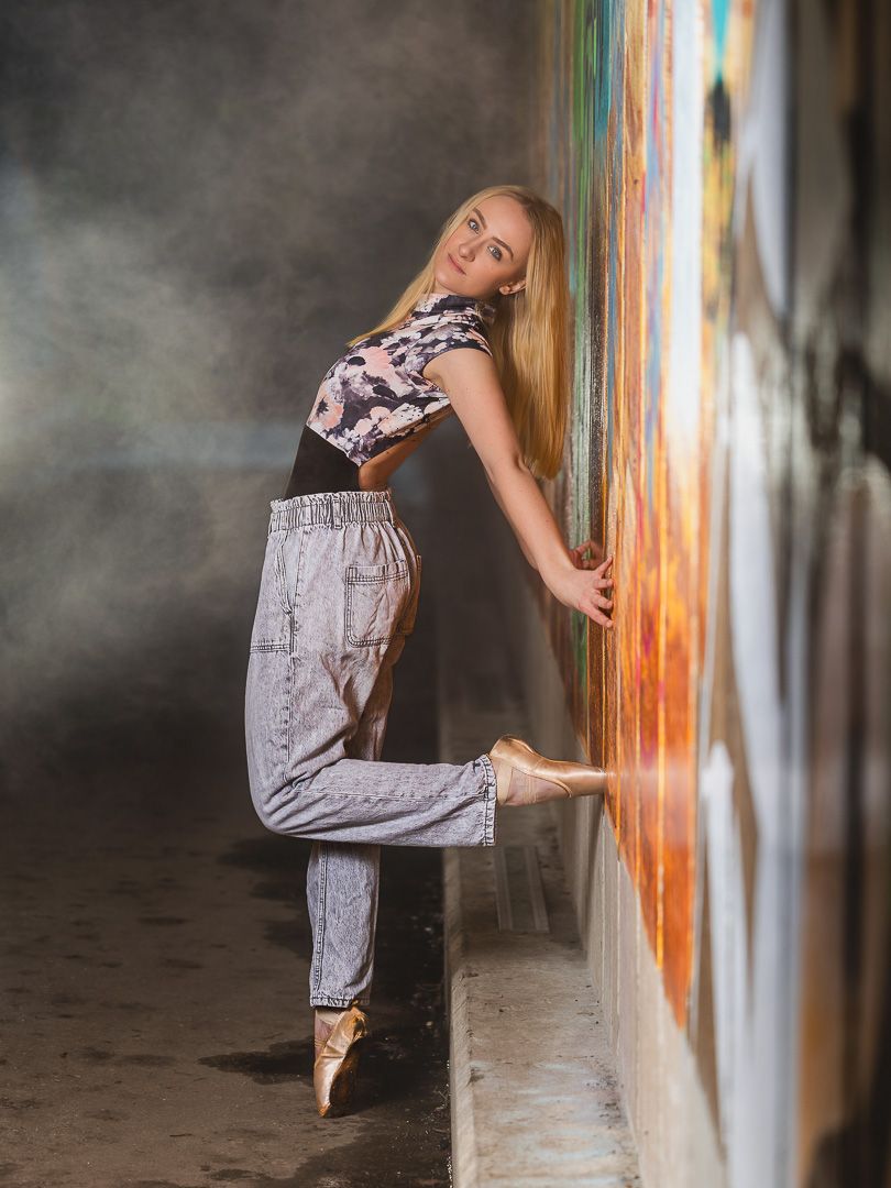 Contemporary dancer in flowing dress performs expressive movements against colorful wall in urban setting.