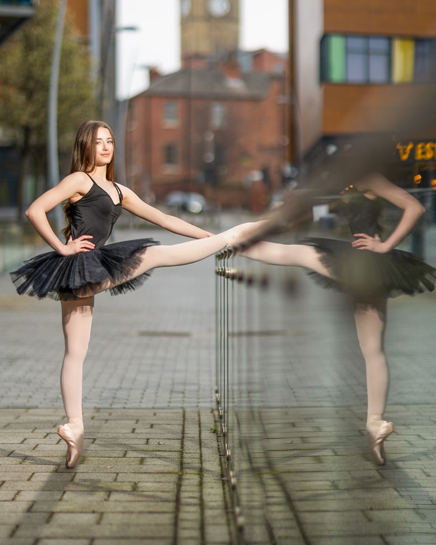 Ballet dancer performs elegant arabesques on urban sidewalk in black tutu.