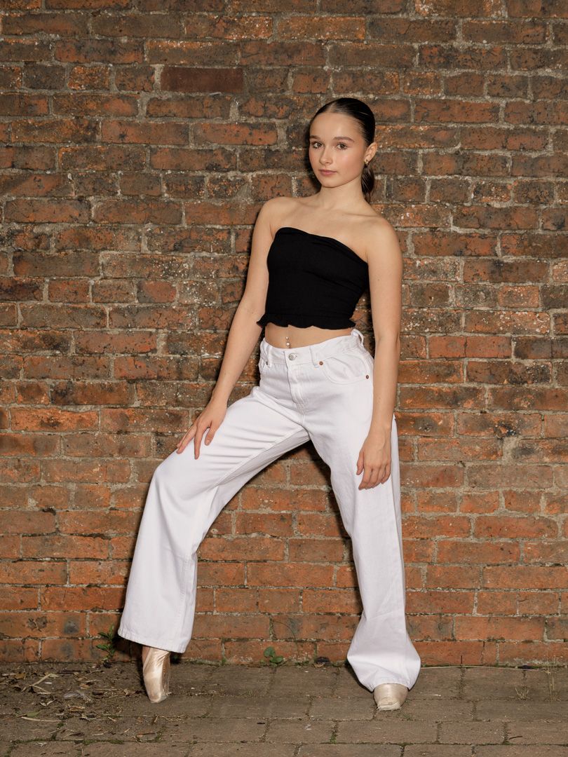 Dance poses against rustic brick wall showcase flowing white pants and black top.