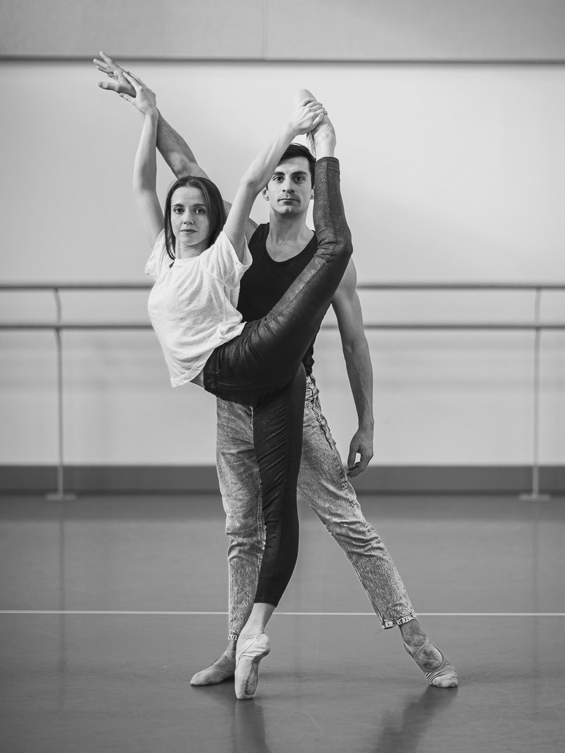 Contemporary dance duet performing synchronized movements in a studio with ballet barre.