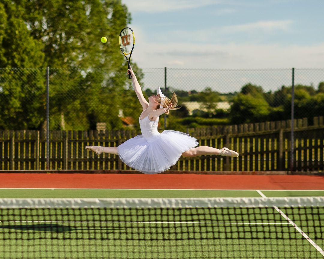 Ballerina in white tutu leaps gracefully with tennis racket on court.