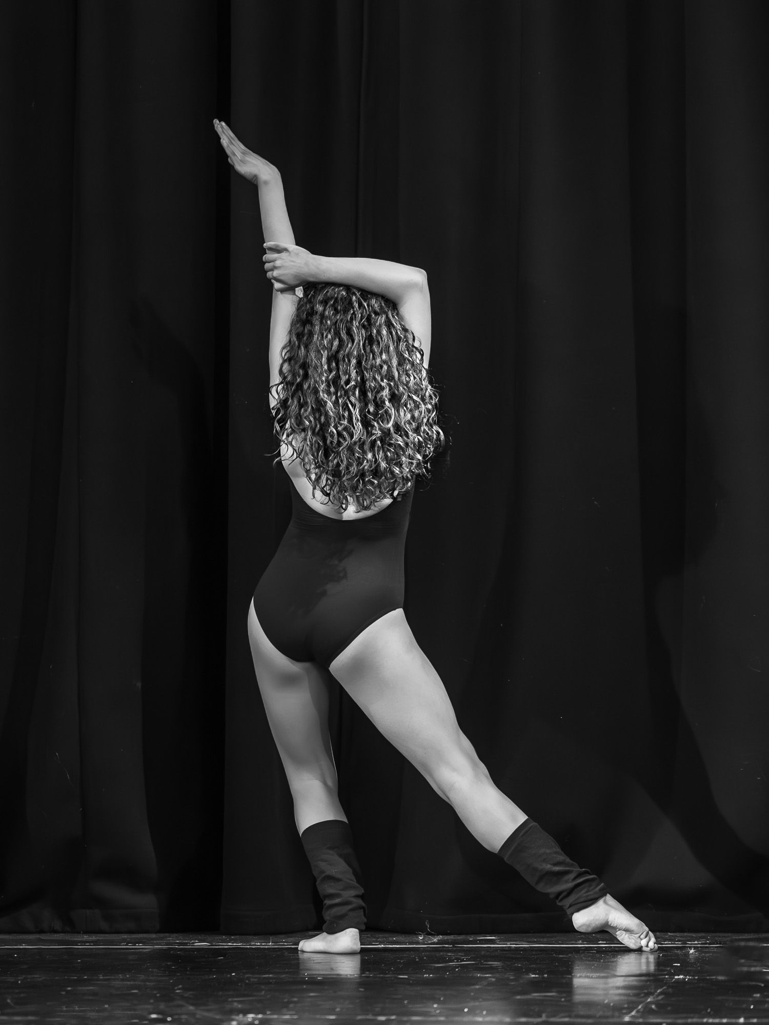 Contemporary dancer in black attire performs low movement sequence on stage.