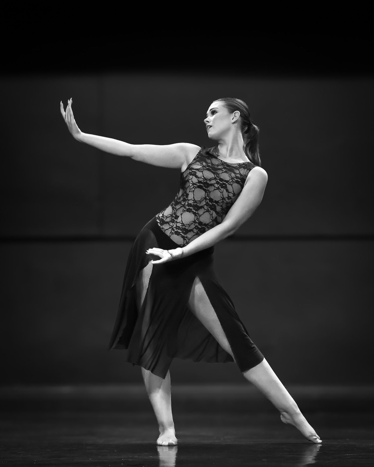 Black and white photo of a female dancer performing a contemporary dance pose on stage in a lace costume.