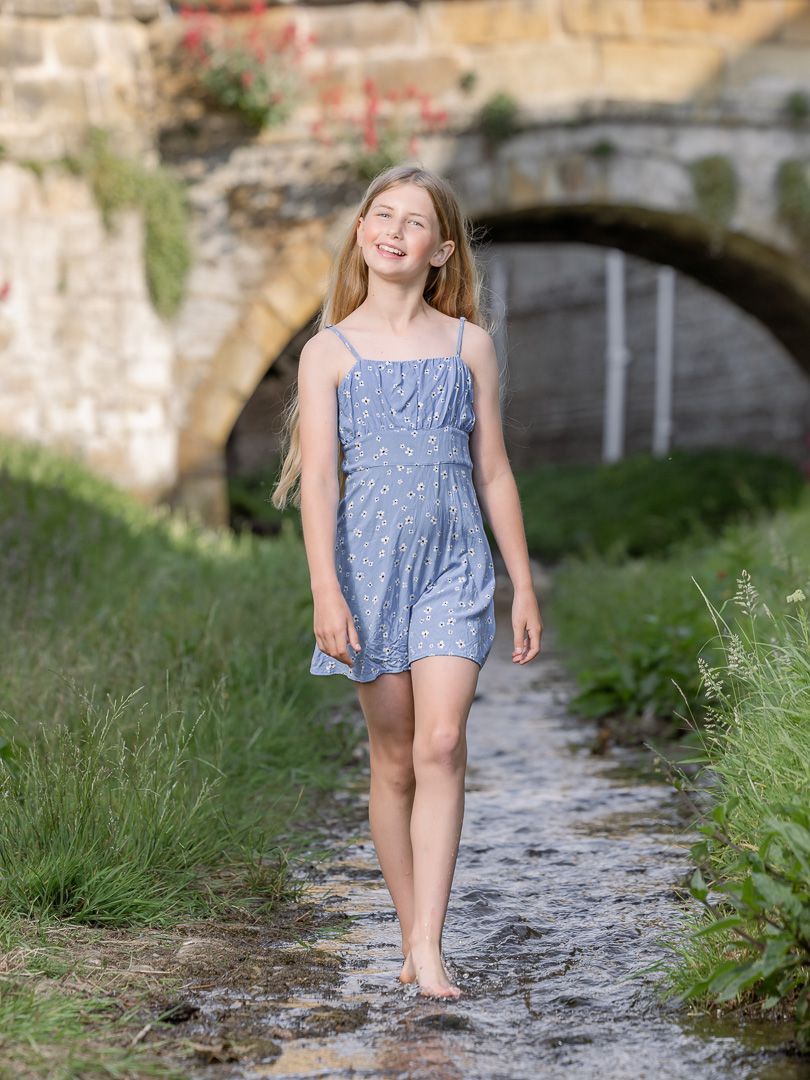 A light blue summer dress worn outdoors near a stone bridge and pathway surrounded by greenery.