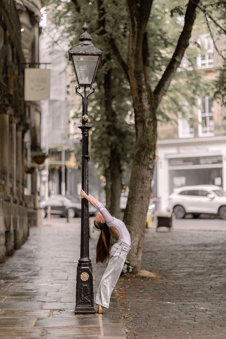 Dancer bends backwards against a vintage street lamp on a cobblestone path.