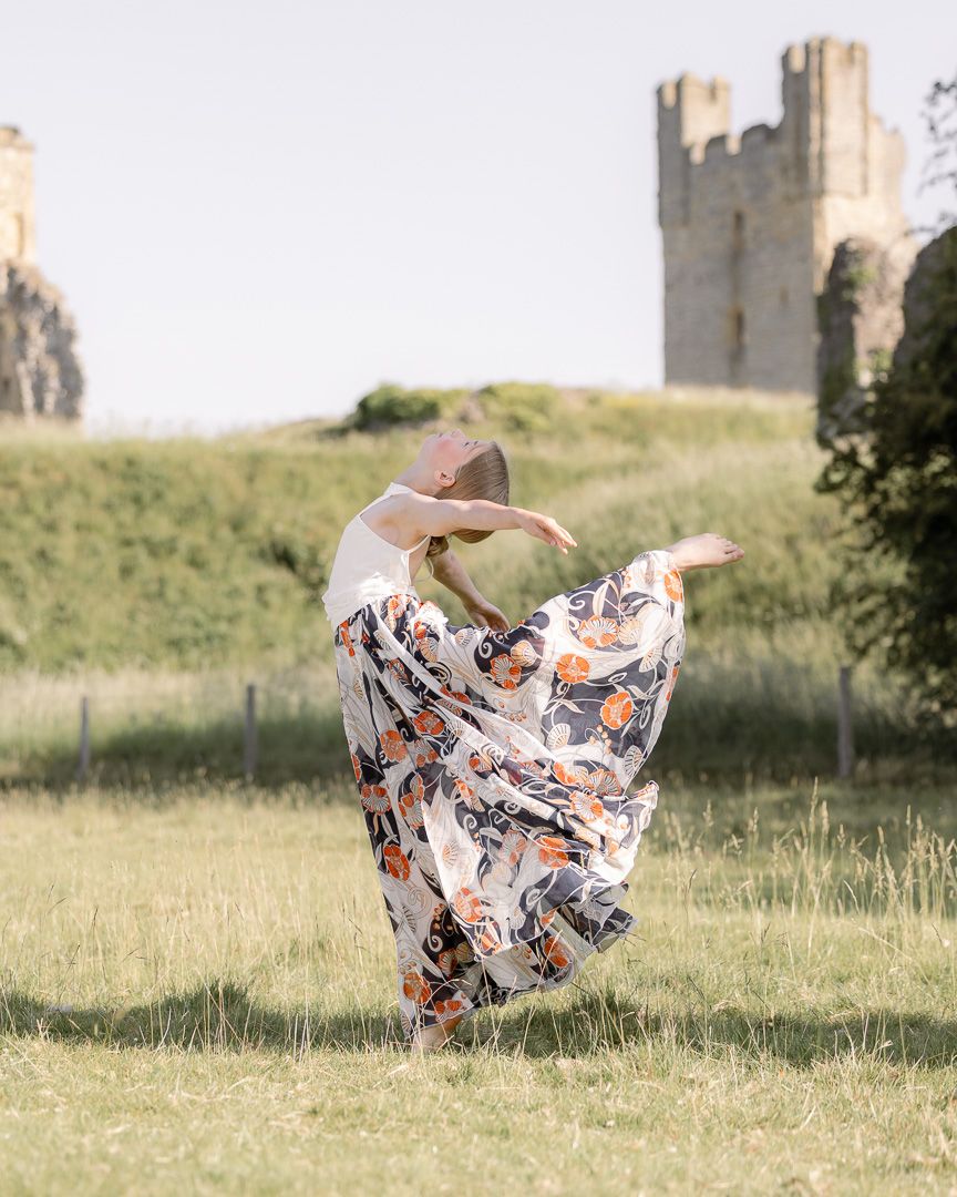 Flowing floral dress twirls during dance performance in front of historic castle ruins.
