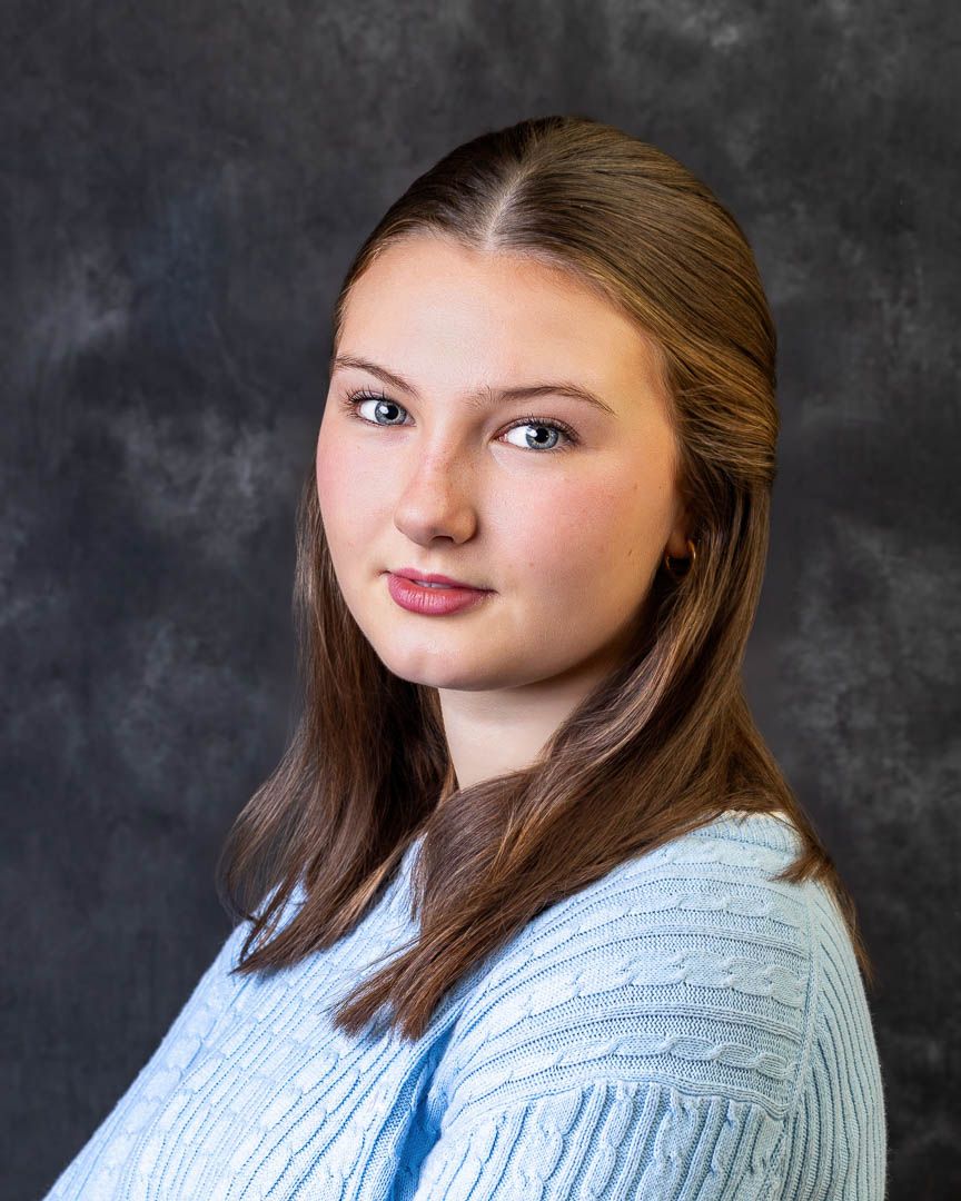 Young woman with long brown hair in light blue sweater poses for professional studio portrait photo.