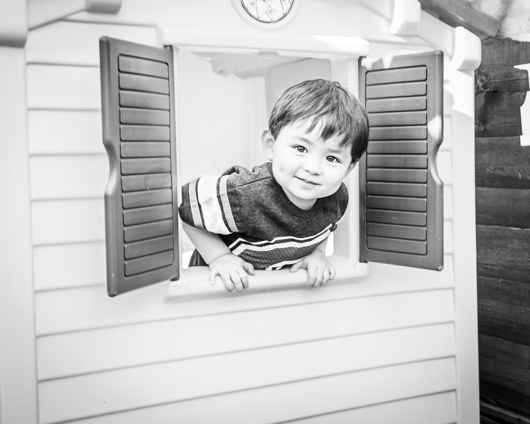 Black and white images of someone peeking through windows of what appears to be a playhouse structure.