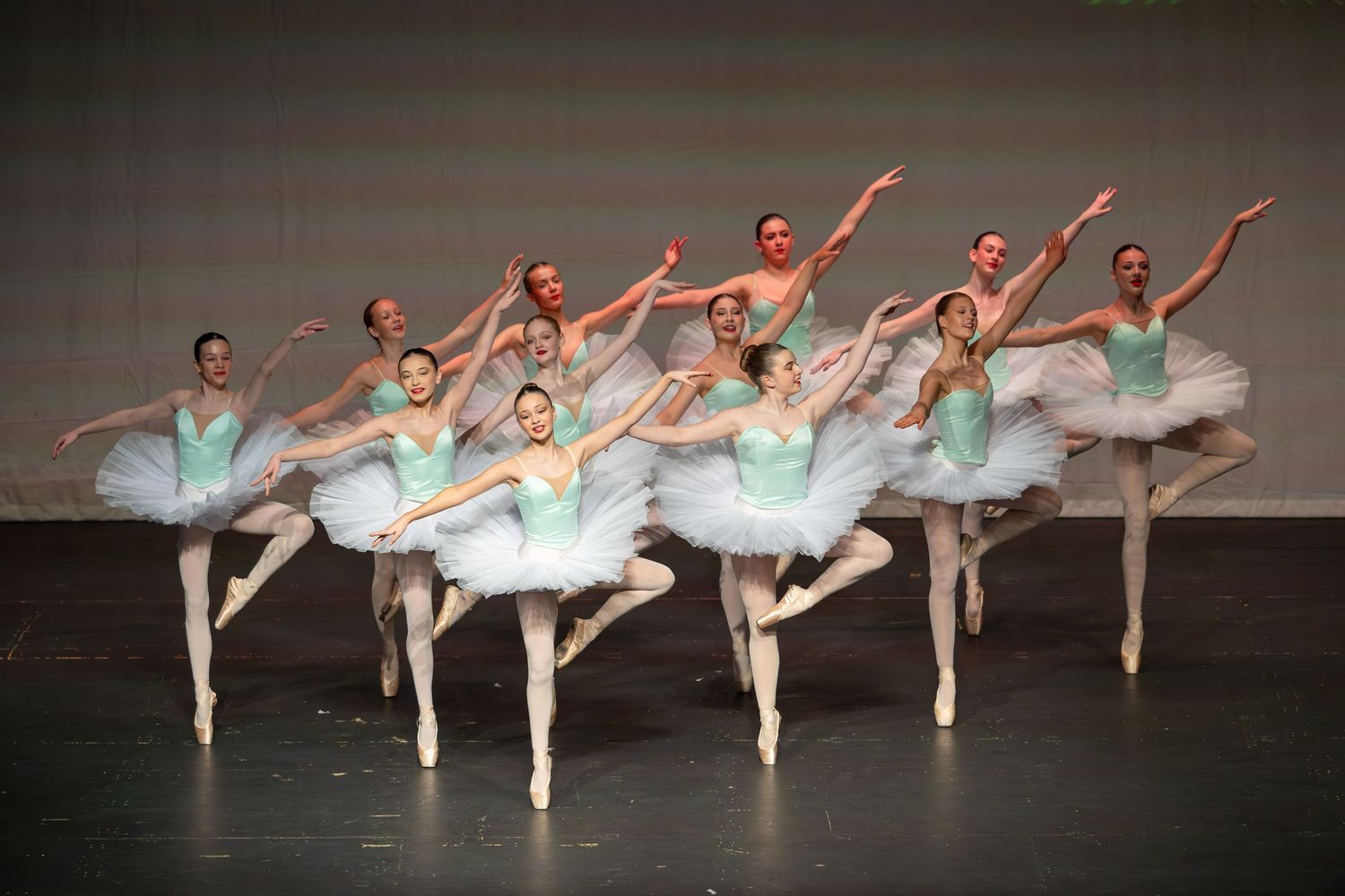 Ballet dancers in white tutus and green bodices perform on stage.