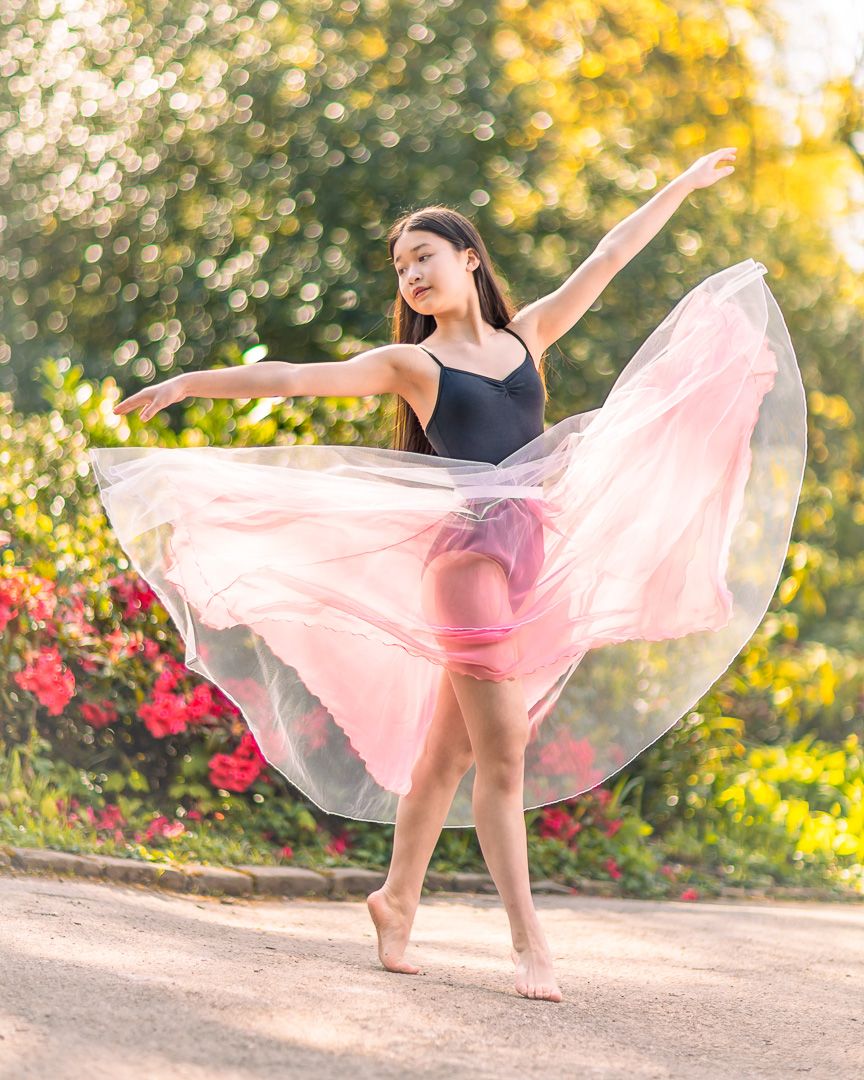 Dancer in pink flowing dress performs graceful movements in garden setting.