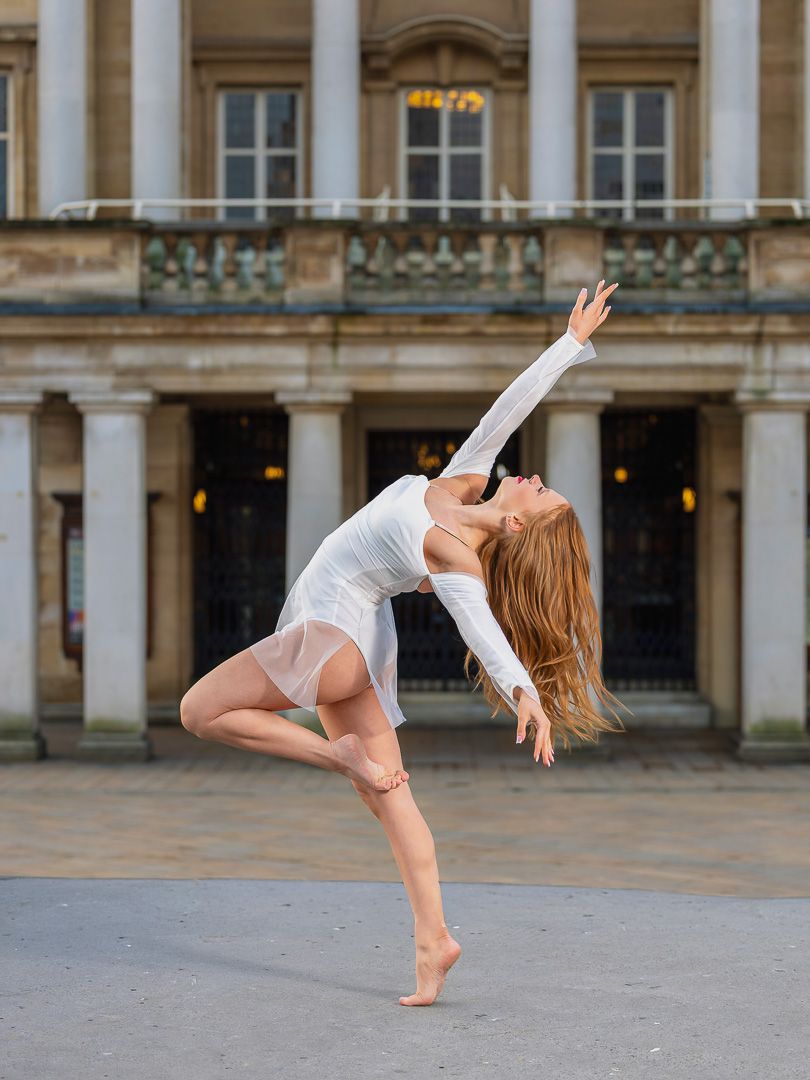 A graceful dancer performs a dynamic sequence of contemporary dance movements against a historic architectural backdrop.