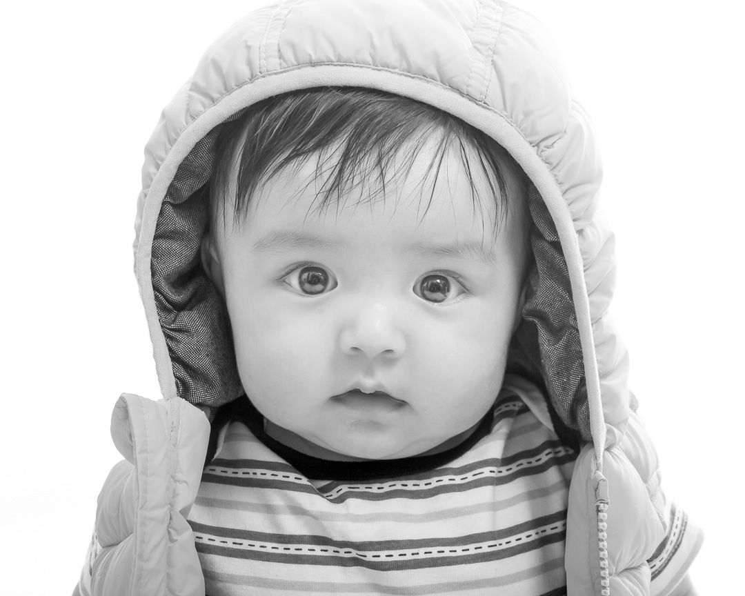 Black and white portrait of a baby wearing a hooded winter coat and striped shirt.