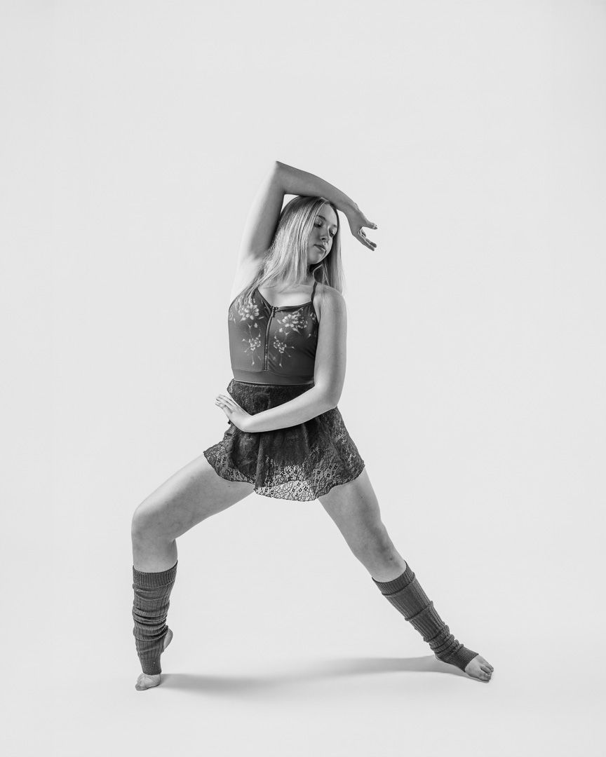 Dancer in patterned dress and leg warmers performs contemporary movement with side stretch.