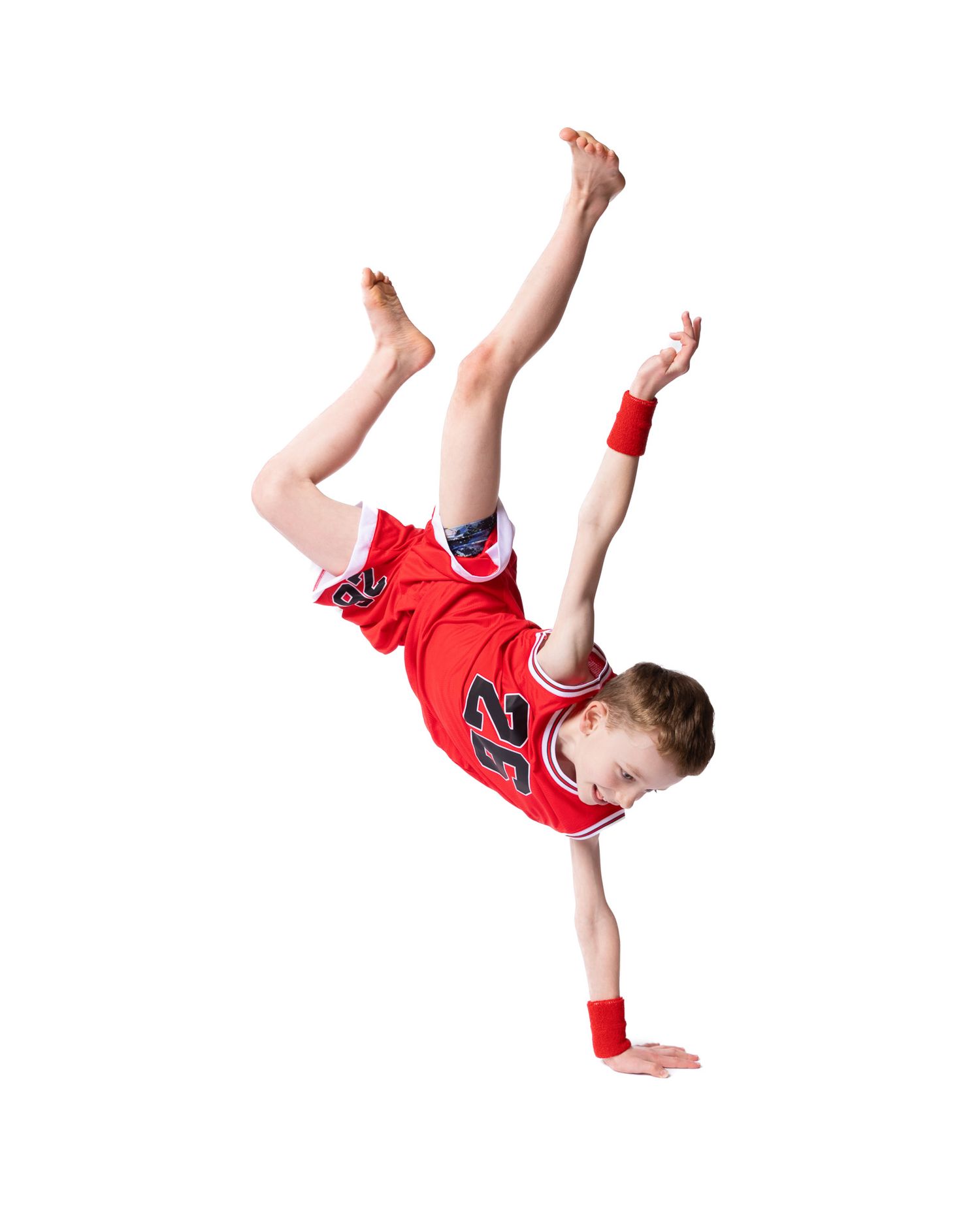 Young dancer performs a one-handed breakdance freeze move in red athletic wear.