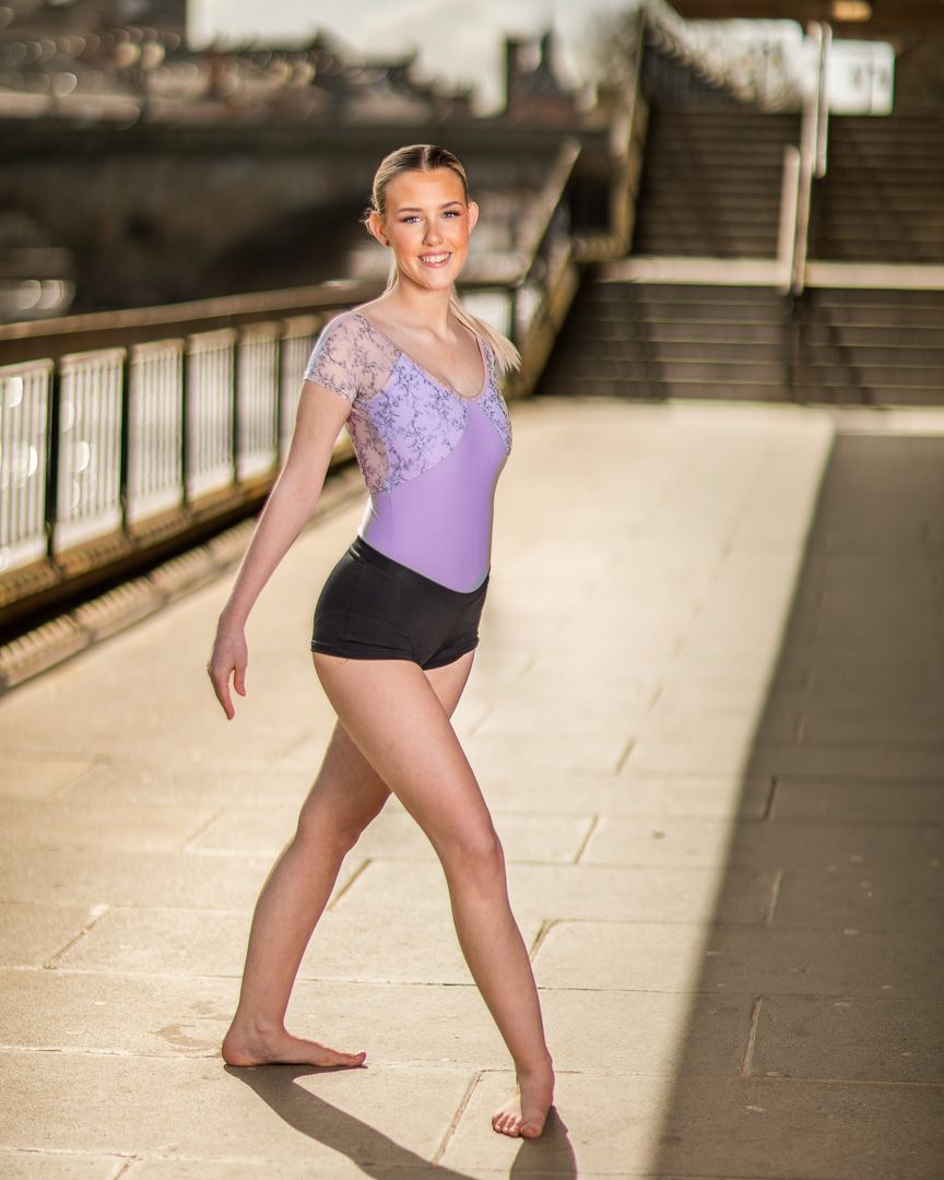 Dancer performs graceful movements on stone steps in purple leotard.