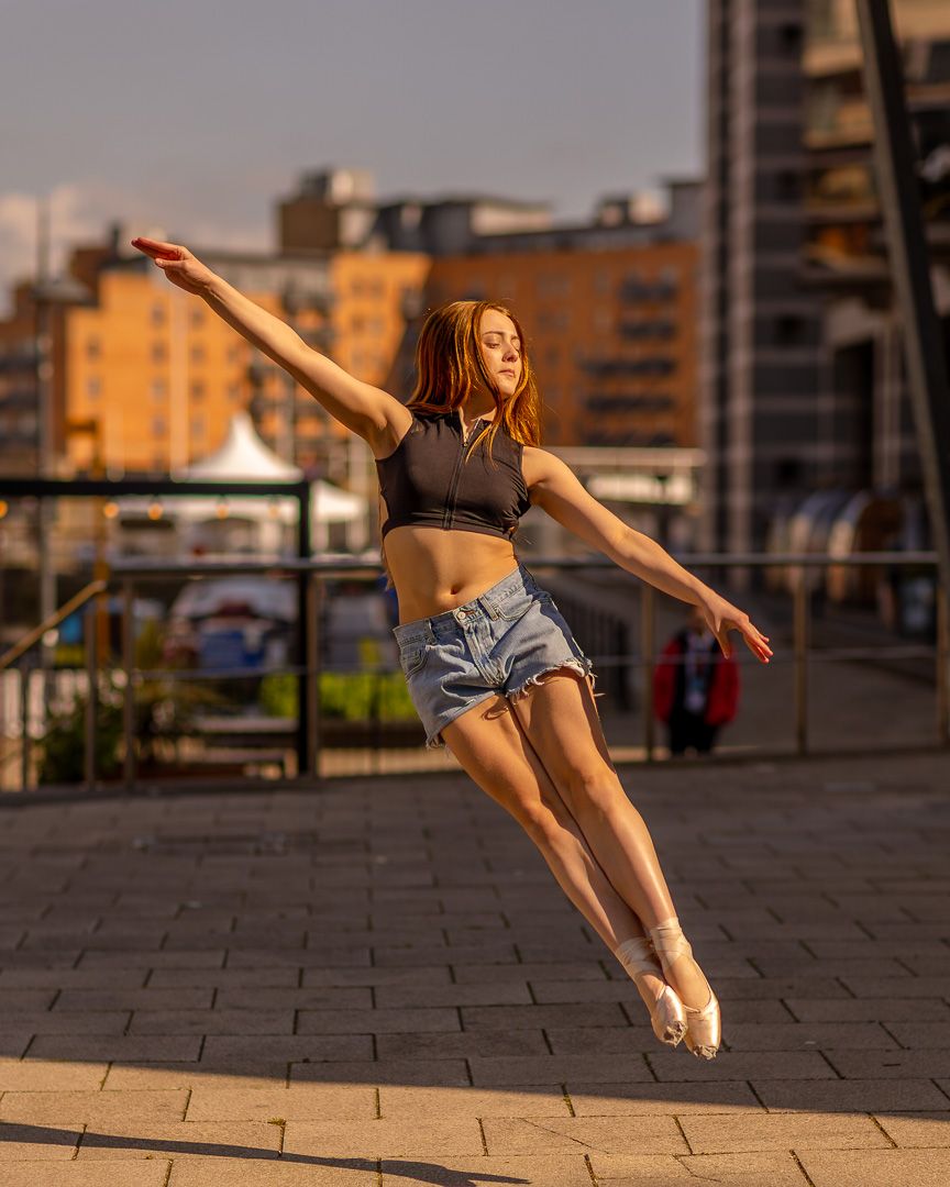 Dancer performs graceful movements on urban rooftop during golden hour.
